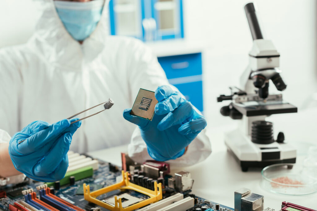 Cropped view of engineer holding microchip and small stone near microscope and computer motherboard